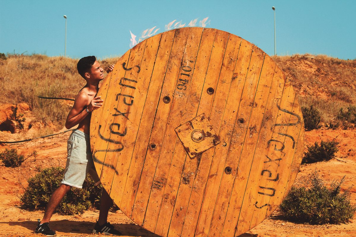 A man doing hard work pushing a huge wooden wheel